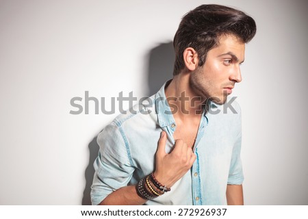 Side view of a young fashion man leaning on a wall while pulling his collar.