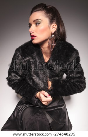 Casual fashion woman closing her fur jacket while looking away from the camera.