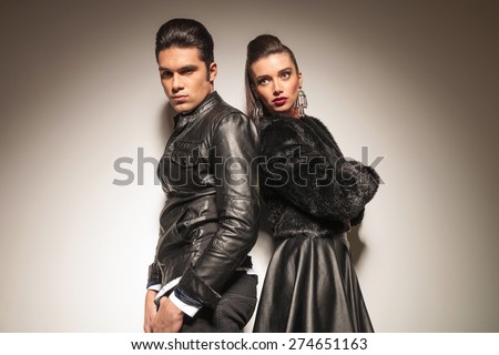 Fashion man and woman standing back to back on grey studio background.