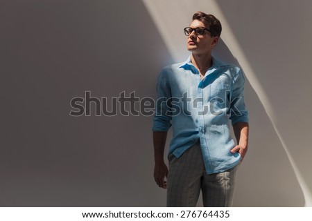 Attractive young casual man looking up while leaning on a wall with his hand in pocket.