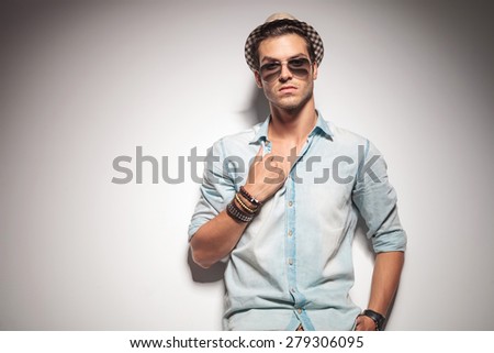 Handsome young fashion man leaning on a studio wall while pulling his shirt.