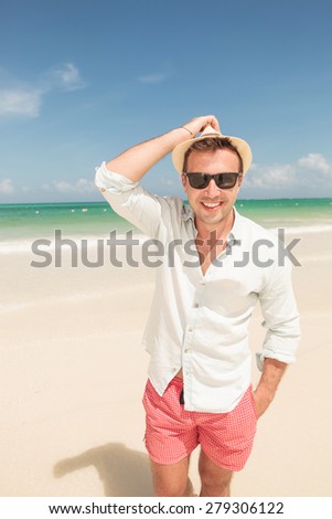 Happy young man walking on the beach holding his hand in pocket, smiling at the camera.