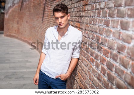 Attractive young fashion man leaning on a brick wall with his hand in pocket.