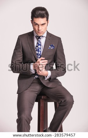 Portrait of a business man sitting on a stool holding his hands together.