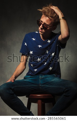 side view of a fashion man fixing his  messy hair while  sitting on a stool in studio