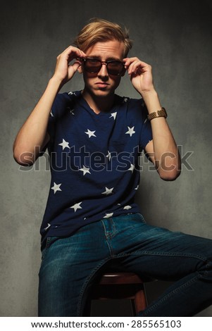 seated fashion man is taking off his sunglasses, studio picture