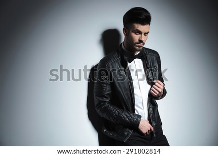 Side view picture of a casual business man leaning on a wall while pulling his leather acket.
