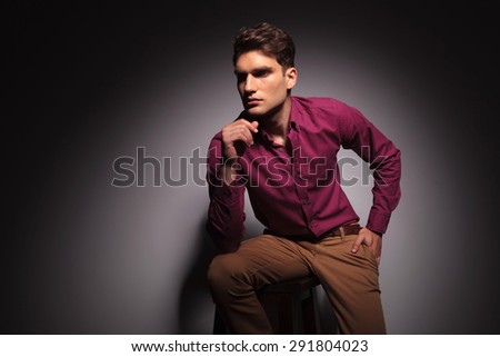 Side view of a young handsome man sitting on a stool with one hand in his pocket.