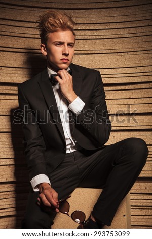 Portrait of a young business man fixing his bow tie while looking away from the camera.