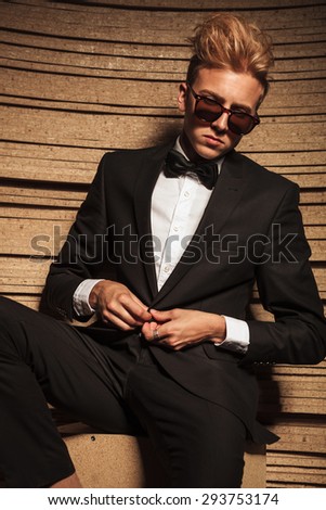 Blond young business man closing his jacket while looking down.