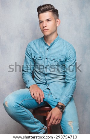 Casual young man sitting on a stool while looking away from the camera.