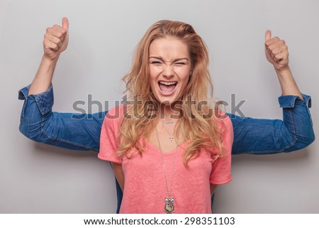 Young blonde woman screaming while her lover is standing behind her showing the thumbs up gesture with both hands.