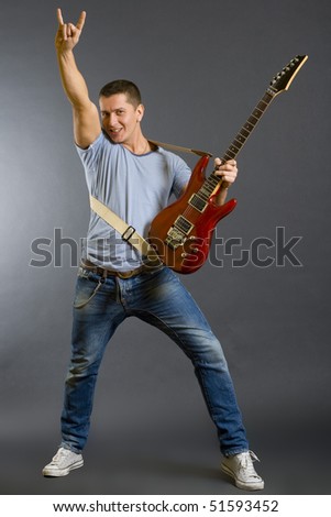 Portrait of a successful rock star holding an electric guitar and making a rock sign on a dark background