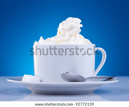 coffee and cream on blue background. cup of coffee with cream on top, little spoon and sugar