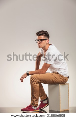 young man in white shirt looking away while seated on a box