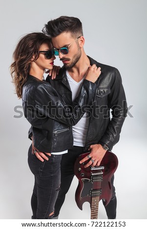 in love rock and roll couple with electric guitar standing embraced on grey studio background