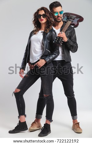 rock and roll man with guitar on shoulder embracing his woman; cool punk couple on grey background