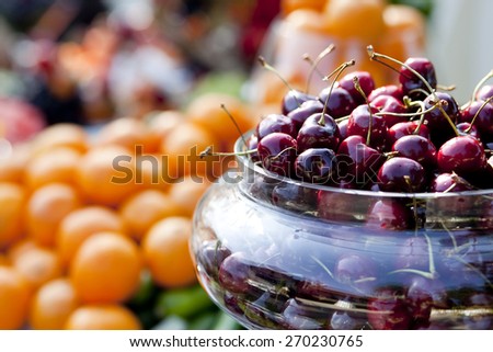 A closeup of a bowl of cherries on an outdoor table of fruit