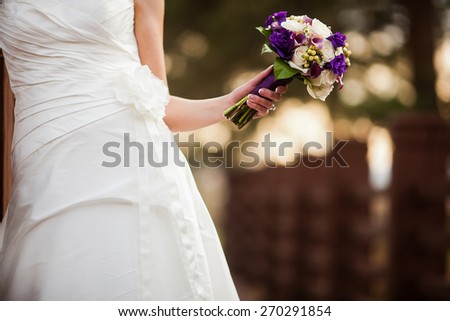 Bride holding wedding Bouquet flowers with purple lisianthus, mini calla lilies, roses, hypericum, and salal leaves