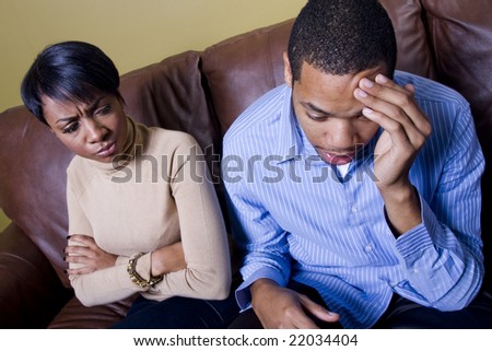 stock photo : A couple is having an argument on a couch and the man is frustrated or feeling guilty