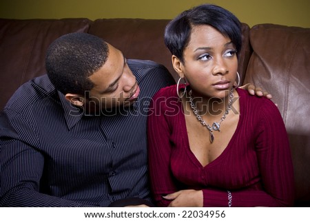 An african american man attempts to cheer up his sad girlfriend on the couch