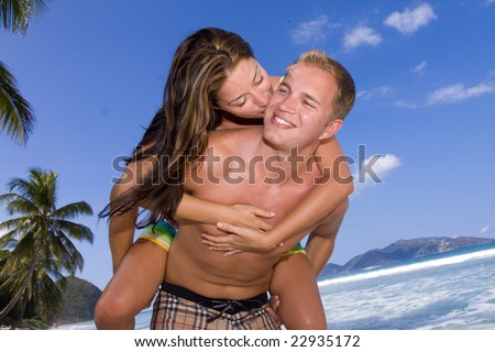A happy girl gives her lover a kiss on the cheek while she rides piggyback on the beach