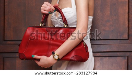 Fashionable sexy woman posing in elegant white dress with red leather handbag in hands