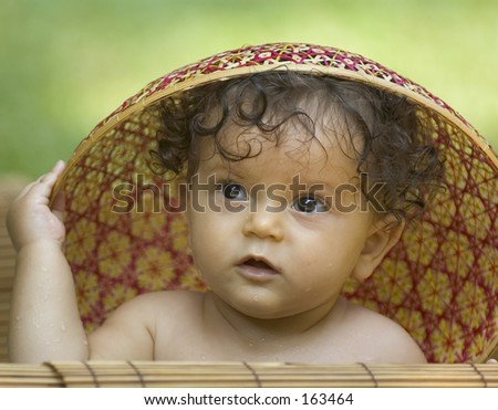 Infant in a tropical garden playing with a vietnamese hat