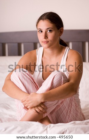 A naturally beautiful young woman sits on a bed in her pyjamas