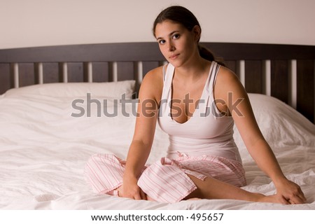 A naturally beautiful young woman sits on her bed at home