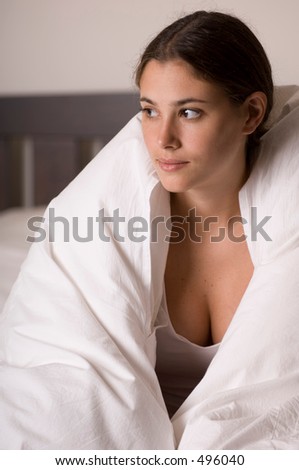 A naturally beautiful young woman sits on her bed looking away from the camera