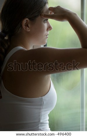 A naturally beautiful young woman looks out of a window holding her head