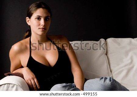A naturally beautiful young woman sits on a white sofa against a black background