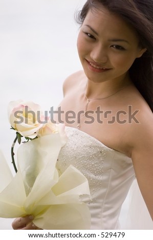 A beautiful asian woman in a wedding dress poses by the side of lake with a yellow rose