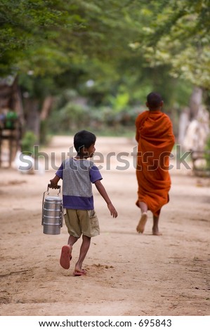 A young boy runs after a monk with a tiffin carrier