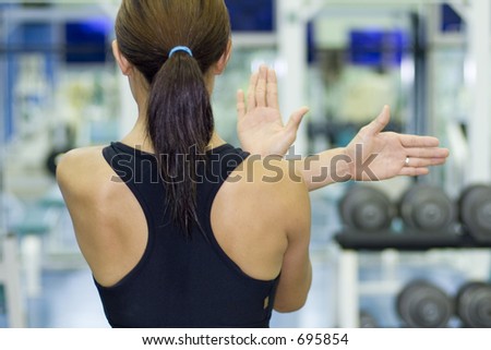 A female fitness instructor demonstrates a shoulder stretch in a gym