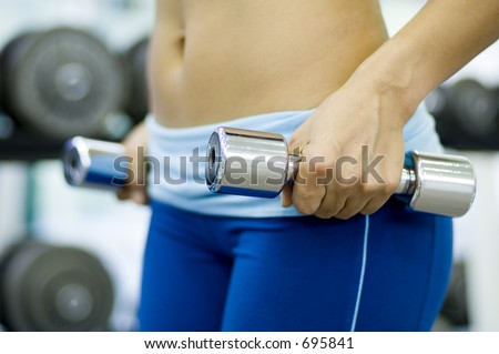 A female fitness instructor holds a pair of chrome dumbbells in the gym