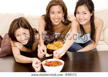 Three attractive asian women eating chips on the sofa