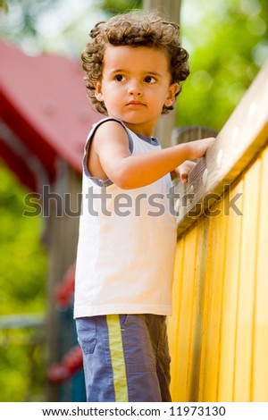 A cute young kid playing on a climbing frame in a park