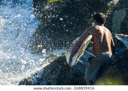 Male surfer walks towards crashing waves while holding his surf board