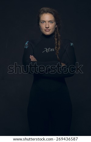Young Caucasian woman in wetsuit looking at viewer with neutral expression with crossed arms