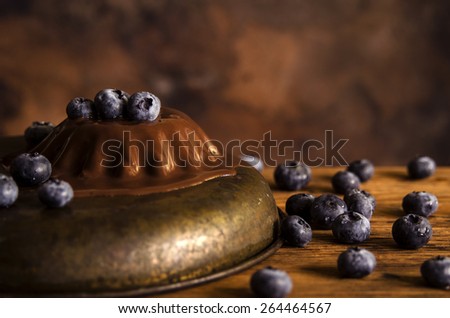 Chocolate panna cotta (italian dessert) with blueberries on dark brown background and wooden table.