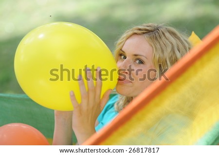 Young attractive woman lying in hammock blowing up yellow balloon