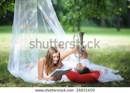 young couple under veil on meadow, man playing trumpet