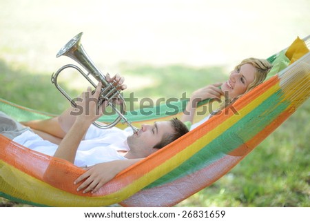 Young smiling woman and man playing trumpet laying in hammock