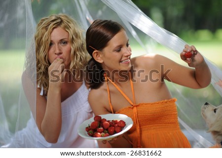 Two smiling women feeding little dog with strawberry