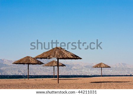 Sunshades near on beach of the Read Sea in Aqaba, Jordan. City of Eilat, Egypt in background.