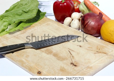 knife on a wood cutting board with vegetables