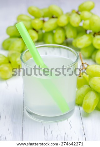 Glass of white grapes juice and grapes on background