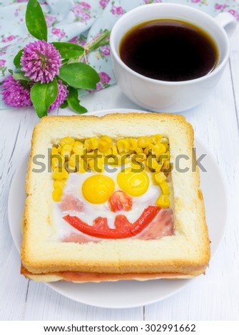 Funny face on baked sandwich, made from cheese, ham, eggs, tomato and corn